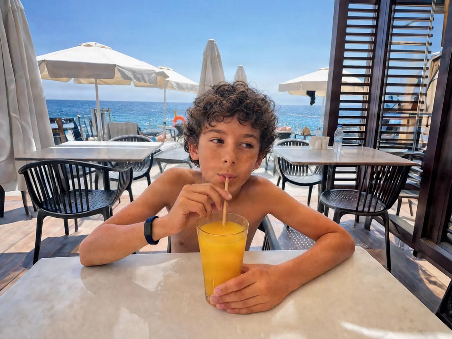 Boy drinking an icy juice at a seaside table, wearing a RUBENPAY LOOP on the wrist